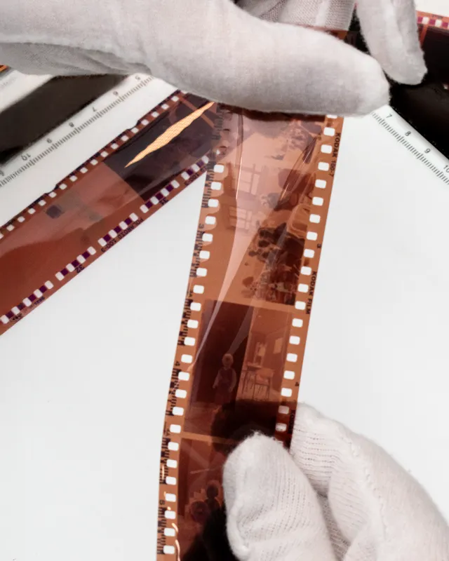Técnico con guantes examinando negativos fotográficos en una mesa de luz